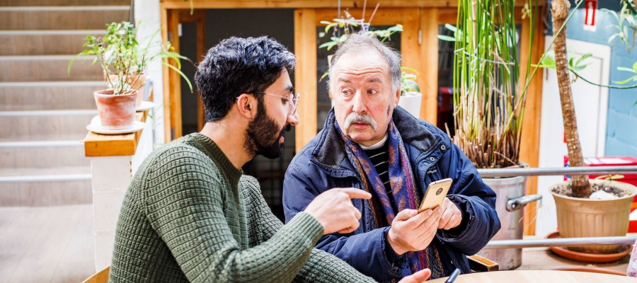 man geeft andere man uitleg over gebruik smartphone